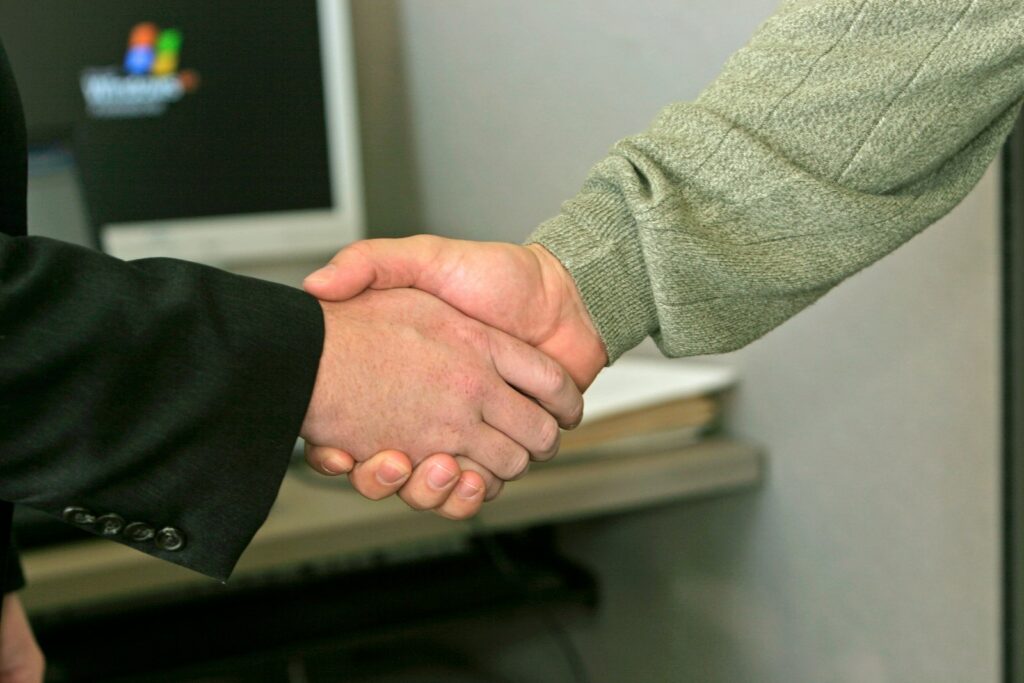 Linkaufbau durch Partnerschaften: zwei Personen geben sich vor einem Monitor die Hand