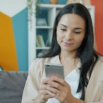 Meta Ads erreichen Nutzer am Smartphone: Frau schaut auf dem Sofa auf ihr Handy